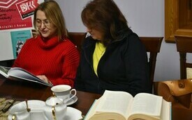 Dwie kobiety siedzą obok siebie, na stole otwarta książka.