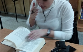 Nastolatka siedzi i ma otwartą książkę, dziewczyna pochyla się nad nią.