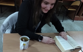 Nastolatka ma otwartą książkę, obok niej kubek z napojem.