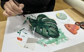 Kobieta maluje zieloną farbą gliniany liść monstery