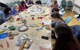 Grupa kilkunastu kobiet siedzi lepi dekoracje z gliny siedząc przy dużym stole