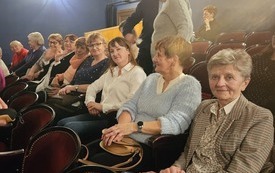 Grupa kobiet siedzi w jednym rzędzie na widowni teatru.