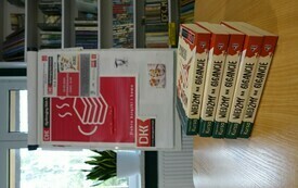 Książki na stoliku, za nimi tablica z logo DKK.