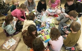 Grupa dzieci siedzi na podłodze i przegląda kolorowe gazety.