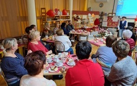 Kobieta w koszuli i kamizelce przemawia do zgromadzonych uczestników spotkania.