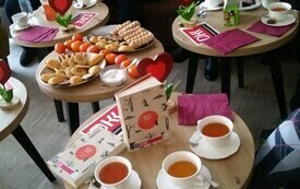 Cztery okrągłe stoliki, na nich ciastka, filiżanki z herbatą, wazony z kwiatami, książki.