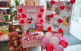 Walentynkowy kącik książkowy, a wnim stolik z książkami, pluszowy miś i kolorowe baloniki