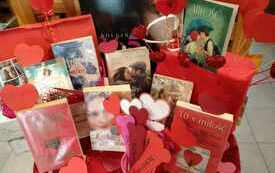 Zbliżenie na książki leżące na nakrytym na czerwono stoliku, obok książek zakładki z motywem serca i papierowe serca na patyczkach
