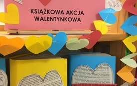 Zbliżenie na książki zapakowane w kolorowy papier, z nalepionymi na okładce sercami wyciętymi z zadrukowanego tekstem papieru