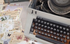 Stara maszyna do pisania, obok niej książki i kolorowe arkusze papieru