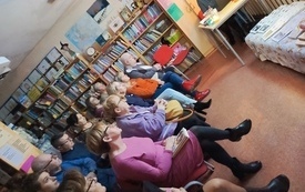 Grupa ludzi zebranych na spotkaniu w bibliotece. Obok gość spotkania.