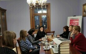 Kilkanaście kobiet dyskutuje przy stole, na którym leżą książki.