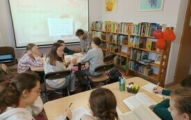 Na prezentacji wyjaśnienie związku frazeologicznego. Przy stolikach grupy uczni&oacute;w z książkami, pracują nad tekstem. 
