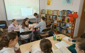 Na prezentacji wyjaśnienie związku frazeologicznego. Przy stolikach grupy uczniów z książkami, pracują nad tekstem.