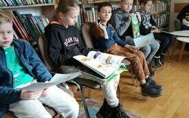 Dzieci siedzą i trzymają w dłoniach książki, kt&oacute;re czytają. 
