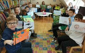 Kilka dzieci siedzi na spotkaniu wokół stołu, w dłonaich trzymają obrazki.
