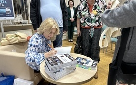 Dziennikarka rozdaje autografy na swoich książkach. Wokół niej zgromadzeni czytelnicy.