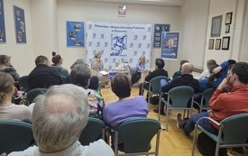 Widownia. Pośrodku sali dwie kobiety na tle ścianki z logo biblioteki.