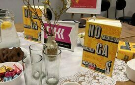 Na stole ksiażki Michała Nogasia, filiżnaka z kawą, flakon i gałązki. W tle plakat DKK.