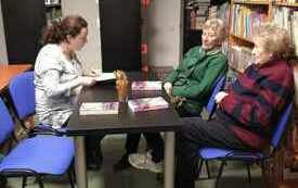 Trzy kobiety siedzą i rozmawiają, po prawej stronie książki. 
