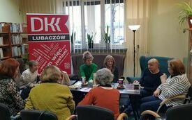 Grupa ludzi wokół stołu, w tle baner Dyskusyjnych Klubów Książki.