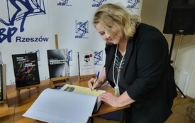 Kobieta w średnim wieku uśmiecha się składając podpis w księdze pamiątkowej biblioteki