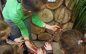 Kobieta trzyma węża, dzieci próbują go dotknąć.