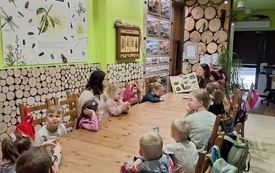 Wnętrze z motywem drewna. Długi stół z siedzącymi przy nim dziećmi.