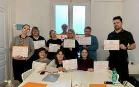 Grupa os&oacute;b pozuje do zdjęcia w sali lekcyjnej trzymając w dłoniach certyfikaty ukończenia szkolenia