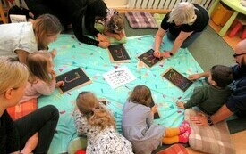 Na dywanie dzieci wraz z rodzicami rysują kolorowe litery.