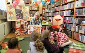 Kobieta w bibliotece pokazuje dzieciom książkę.