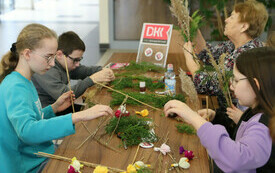 Dzieci tworzą palmę z roślin, papieru, w tle logo DKK.