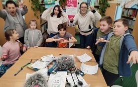 Grupa dzieci i bibliotearka mają podniesione ręce i pokazują groźne miny.