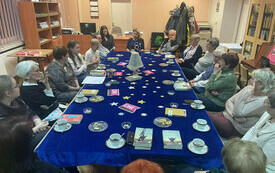 Grupa ludzi w różnym wieku siedzi przy stole i dysutuje.