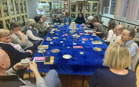 Grupa ludzi siedzi przy stole, na którym jest lampa z papieru.