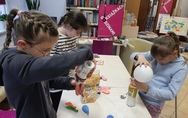Trzy dziewczynki trzymaja balony i wsypują do nich mąkę.