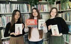 Trzy nastolatki trzymają ksiąki i logo Dyskusyjncych Klubów Książki.