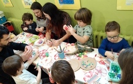 Grupa dzieci i kobieta siedzą przy stole i wykonują prace plastyczne, wycinają, kolorują.