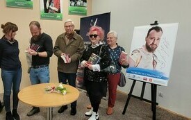 Kilka kobiet dyskutuje przy stole, za plecami plakat.