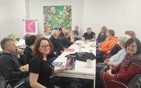 Grupa ludzi rozmawia przy stole, bibliotekarka trzyma książkę w rękach.