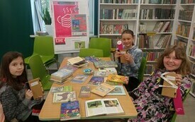 Kilkoro dzieci trzyma książki, w tle plakat Dyskusyjnych Klubów Książki.