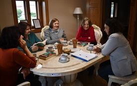 Pięć kobiet siedzi przy stole i rozmawia. 