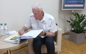 Starszy mężczyzna siedzi przy stoliku i wpisuje się do bibliotecznej kroniki