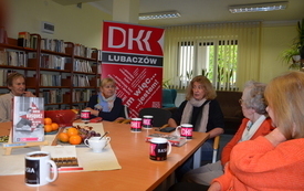 Kilka kobiet siedzi przy stole i rozmawia. W tle baner z logo DKK. 
