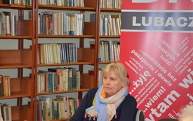 Bibliotekarka na tle regałów i logo DKK.