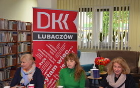 Trzy kobiety siedzą przy stole. W tle baner z logo Dyskusyjnych Klubów Książki Lubaczów.