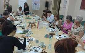 Grupa kobiet w r&oacute;żnym wieku siedzi wok&oacute;ł stołu, na kt&oacute;rym leżą materiały do tworzenia biżuterii
