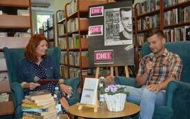 Jakub Małecki trzyma mikrofon i mówi, obok na fotelu siedzi dyrektor biblioteki w Lubaczowie.