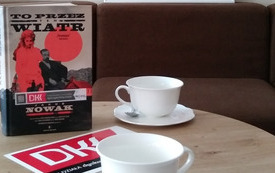Dwie filiżanki na stole, po prawej stronie książka i logo DKK. 