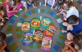 Dzieci siedzą w kręgu na podłodze, pomiędzy nimi leżą książki